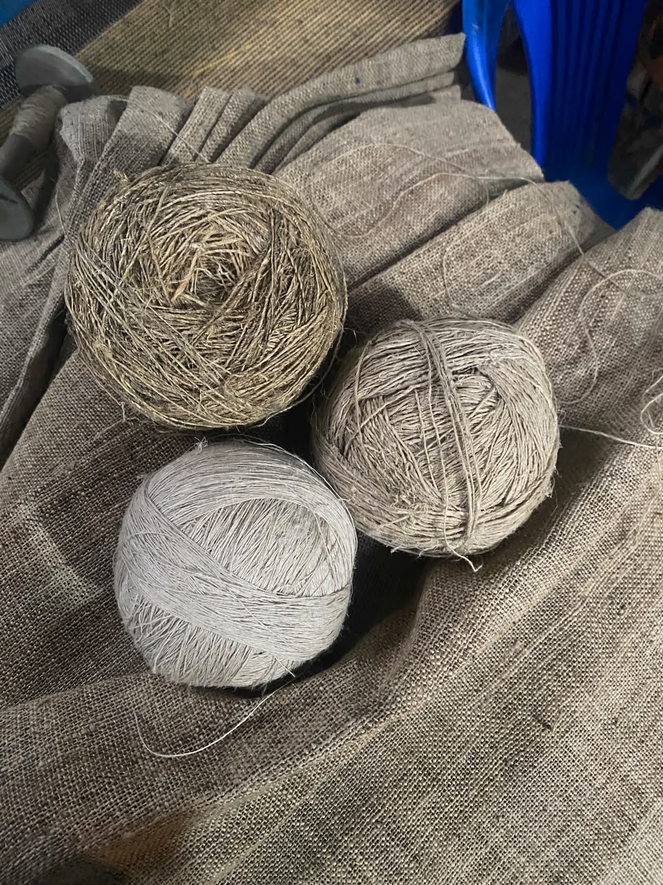Three balls of undyed hemp and banana fibre thread resting on hand-woven cloth