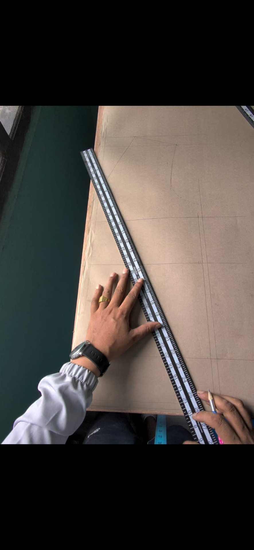 Hands marking a suit pattern on brown paper with a ruler and pencil