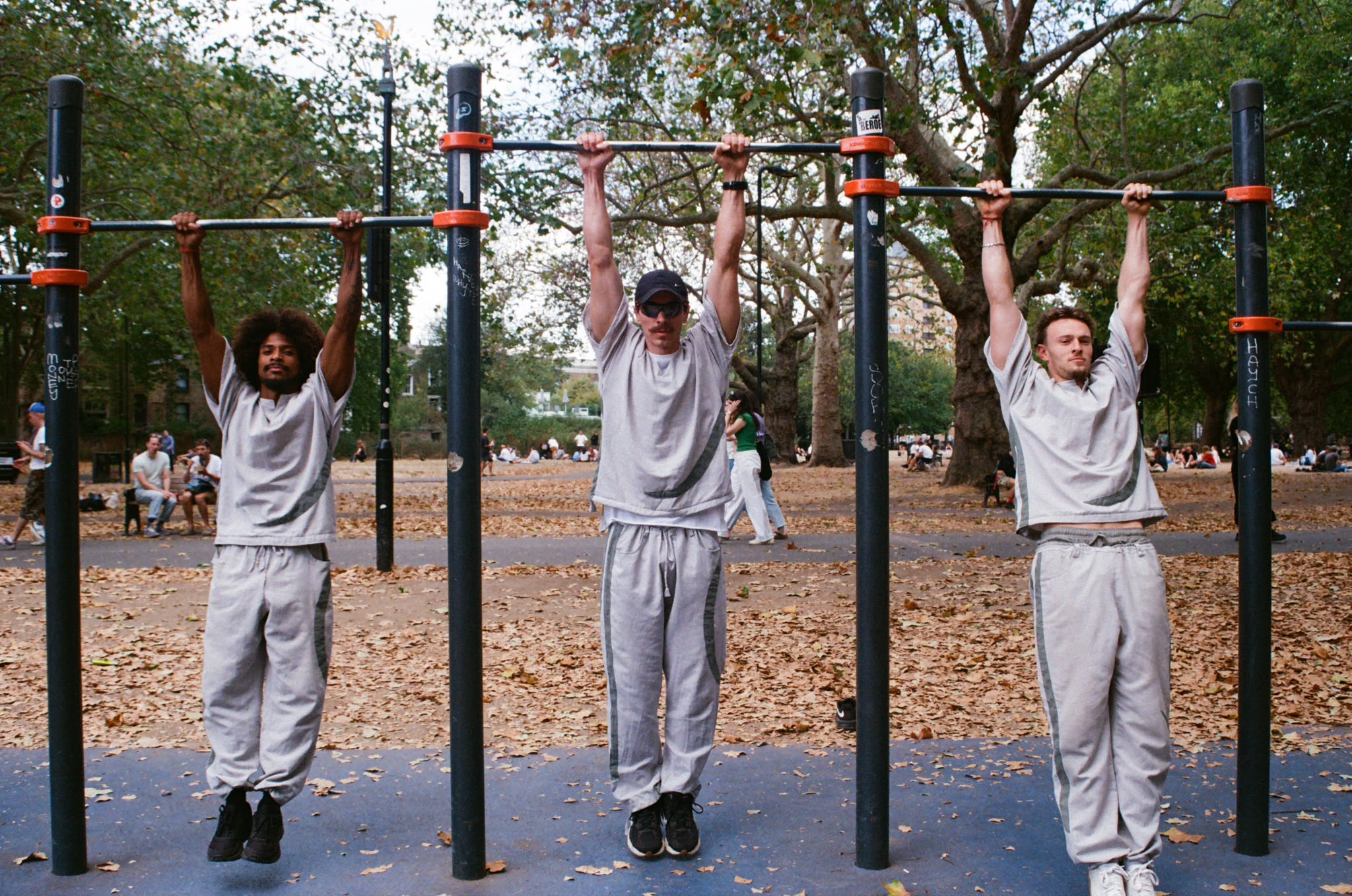 Three people hanging from pull-up bars in a park, wearing matching light grey hemp sets.